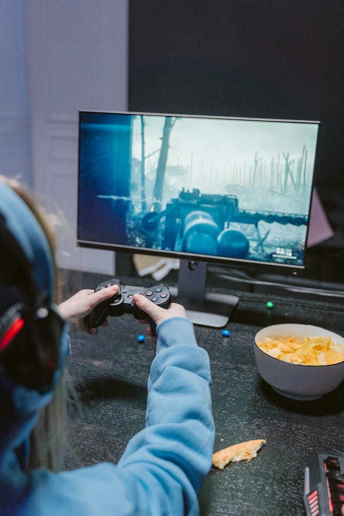 A focused gamer enjoying a shooter game on a monitor with snacks nearby, showcasing a gaming lifestyle.