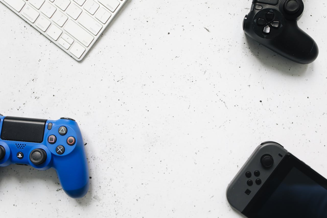 A variety of game controllers and a keyboard arranged on a white textured surface, offering a minimalist gaming setup.